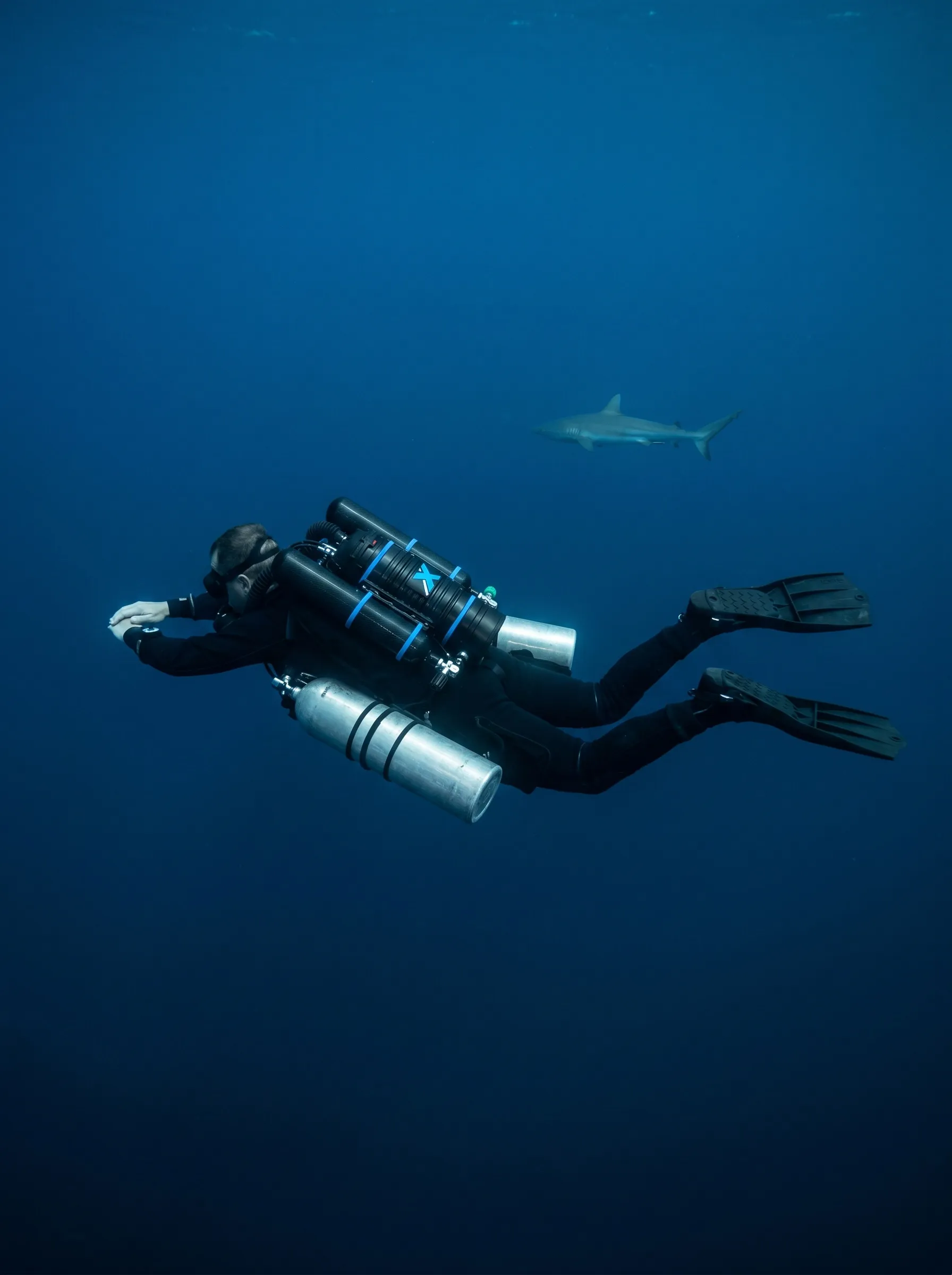 Silhouette d’un plongeur recycleur XCCR à soixante mètres, un requin gris au loin